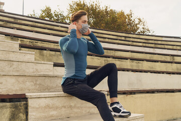 Athletic and handsome young male wearing a gray mask. Young athlete wearing a mask to train outside. Fit muscular sportsman dressed in sportswear wearing a gray mask.