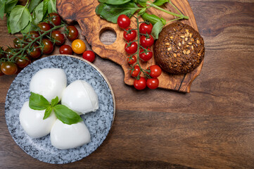 Cheese collection, white balls of soft Italian cheese mozzarella, served with red cherry tomatoes, fresh basil leaves
