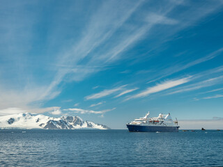 view to passenger vessel in Antarctic waters under blue sky with light clouds and copy space