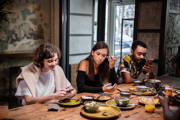 A multicultural group of students sharing food in a cafe and using free wifi, texting, listening to audio-messages.