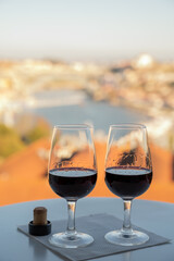 Tasting of different fortified dessert ruby, tawny port wines in glasses with view on Douro river, porto lodges of Vila Nova de Gaia and city of Porto, Portugal