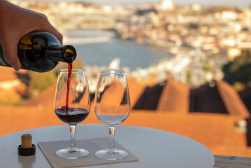 Pouring of fortified dessert ruby, tawny port wines in glasses with view on Douro river, porto lodges of Vila Nova de Gaia and city of Porto, Portugal