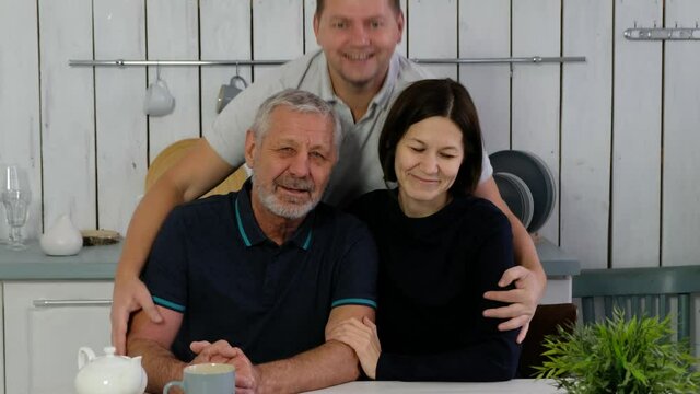 Senior beared man, adult son and daughter at the kitchen smiling happily anf hugging, happy family