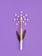 Bamboo toothbrush, eco toothpaste in tablets and dried plants. Creative shape of flower on a violet...