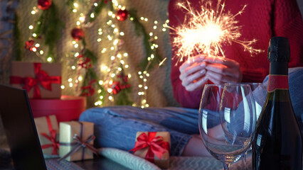 Christmas online family greetings.Woman holding sparkler and champagne in hands wishes friends and family Merry Christmas and Happy New Year by video call during coronavirus pandemic,self-isolation