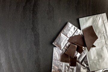 Chocolate ba on black wooden background top view. Chocolate wrapped in aluminum foil on a wooden...