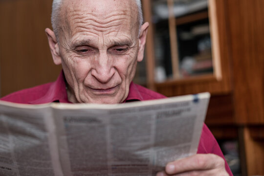 senior man with bad eyesight reading newspaper at home