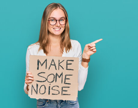 Beautiful blonde woman holding make some noise banner smiling happy pointing with hand and finger to the side