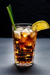 long island ice tee cocktail in a transparent glass on a black background with a garland inside the glass. new year cocktail. vertical image. close-up. frontal shooting