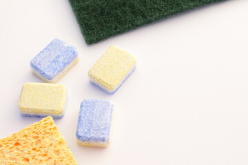 Kitchen sponges and wash machine tablets, yellow and green kitchenware and soap on white, close up isolated domestic wash tool