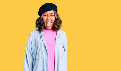 Young beautiful mixed race woman wearing french look with beret sticking tongue out happy with funny expression. emotion concept.
