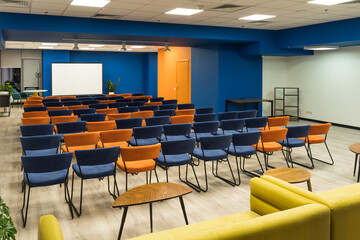 Conference hall with orange and blue chairs and blank screen