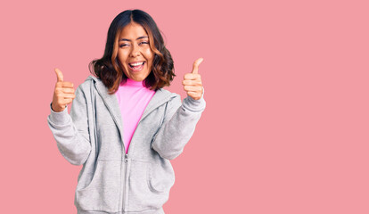 Young beautiful mixed race woman wearing casual sporty clothes success sign doing positive gesture with hand, thumbs up smiling and happy. cheerful expression and winner gesture.