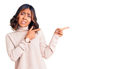 Young beautiful mixed race woman wearing winter turtleneck sweater pointing aside worried and...