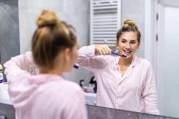 Yooung pretty woman brushing her teeth at mirror