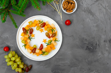 Christmas wreath of snacks made of cheese and grapes on a white plate on a concrete background. Christmas food background concept. Top view.