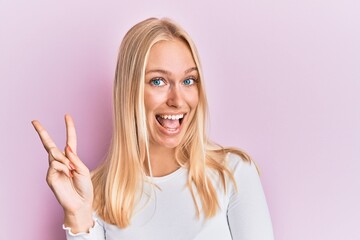 Young blonde girl wearing casual clothes smiling with happy face winking at the camera doing victory sign. number two.