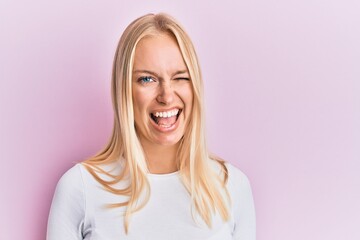 Young blonde girl wearing casual clothes winking looking at the camera with sexy expression,...