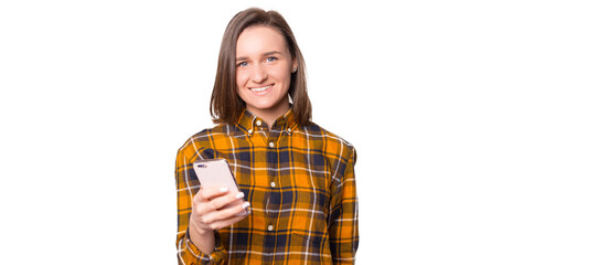 Positive teen female student in casual checkered shirt smiling and looking at camera while using mobile app on smartphone isolated on white background
