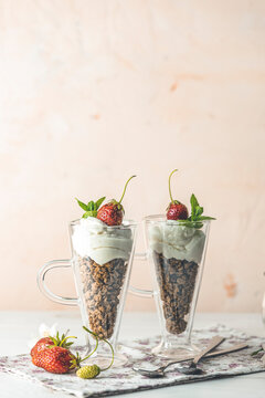 Two glass of healthy breakfast with granola and greek yogurt decorated by mint and raw strawberry served on white wooden background