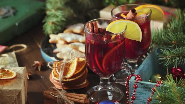 Fragrant, hot punch or mulled wine for Christmas in a tall cup on a background of gifts, toys and fir branches. Hot winter drink of wine with spices and fruit, rotation.