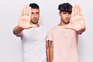 Young gay couple wearing casual clothes doing stop sing with palm of the hand. warning expression with negative and serious gesture on the face.