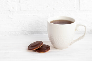 a Cup of black tea white on a white background next to chocolate covered cookies with space for text