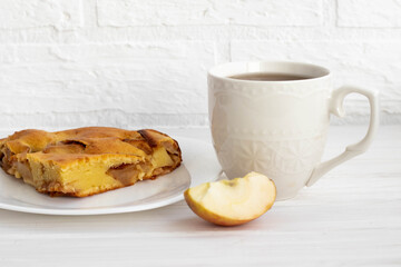 a white Cup with tea next to a piece of delicious ruddy Apple pie on a white plate