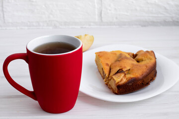 a mug of red tea or coffee next to a piece of Apple pie on a white plate