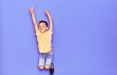 Adorable kid wearing casual clothes jumping over isolated purple background