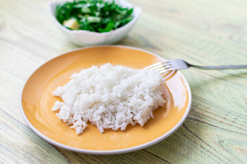 White boiled rice on a plate on a wooden background.
