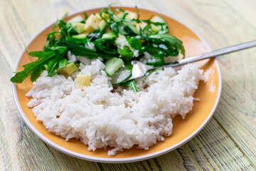 White boiled rice and greens salad on a wooden background. Healthy food concept.