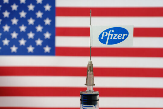 Pfizer vaccine Covid-19 concept. Syringe needle and Pfizer sticker on it, blurred flag of the United States on background. Real photo, not a montage. Stafford, United Kingdom - November 22 2020.