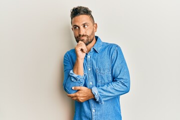 Handsome man with beard wearing casual denim jacket thinking concentrated about doubt with finger on chin and looking up wondering