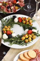 An appetizer of rosemary stuffed with olives with baby mozzarella and cherry tomatoes. Made in the form of a Christmas wreath.