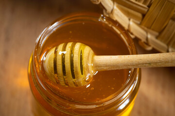 Honey in a glass jar with a wooden honey dipper on a wooden table. Healthy organic honey. Close-up