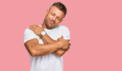 Handsome muscle man wearing casual white tshirt hugging oneself happy and positive, smiling confident. self love and self care