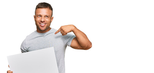 Handsome muscle man holding blank empty banner pointing finger to one self smiling happy and proud