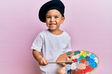 Adorable latin toddler smiling happy wearing artist style using paintbrush and palette over...