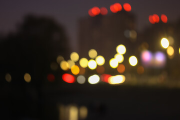 The facade of the apartment building, light in the windows in the evening, blurred houses in the big city and bright colorful abstract lights. 