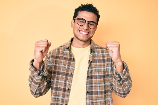 Young handsome hispanic man wearing casual clothes and glasses screaming proud, celebrating victory and success very excited with raised arms