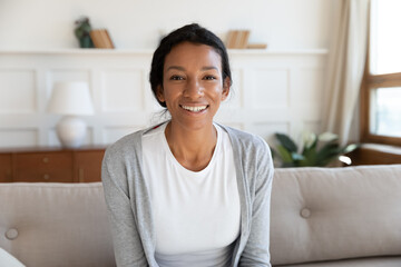 Close up portrait of smiling African American woman sit on sofa at home talk on video call online....