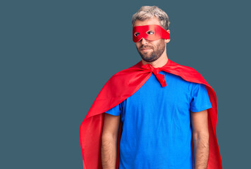 Young blond man wearing super hero custome smiling looking to the side and staring away thinking.