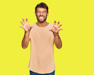 Handsome young man with beard wearing casual tshirt smiling funny doing claw gesture as cat,...