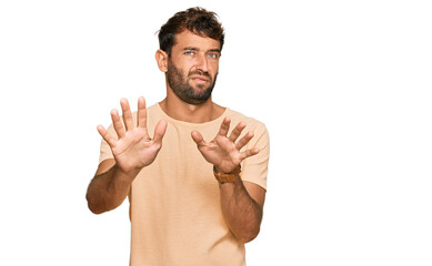 Handsome young man with beard wearing casual tshirt moving away hands palms showing refusal and...