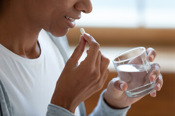 Crop close up of smiling young African American woman take daily dose of vitamin or dietary...