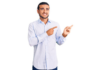 Young handsome man wearing business clothes pointing aside worried and nervous with both hands, concerned and surprised expression