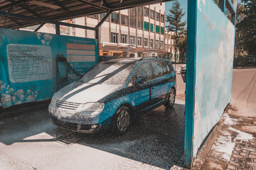 Car wash, a person at a self-service car wash, under a stream of pressure puts foam on the car.