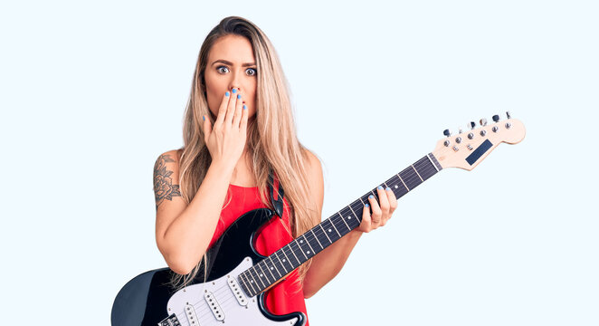 Young beautiful blonde woman playing electric guitar covering mouth with hand, shocked and afraid for mistake. surprised expression