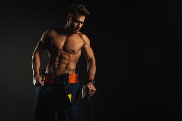 Fototapeta na wymiar young handsome adult, muscular firefighter in uniform holding ax of fire equipment in his hands, pensive, isolated on dark background. Low key. Protection concept. there is a place for an inscription